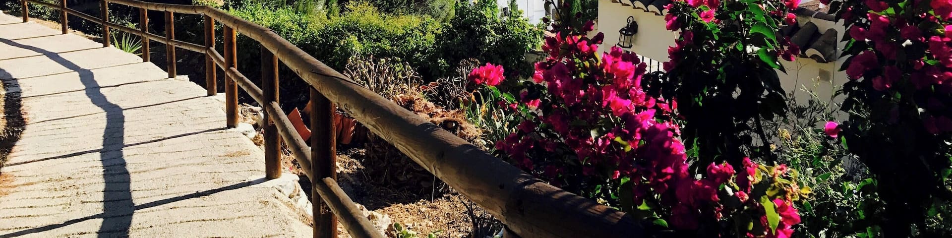 A scenic view of a town nestled in a valley with mountains in the background, a wooden staircase, and vibrant pink bougainvillea flowers.