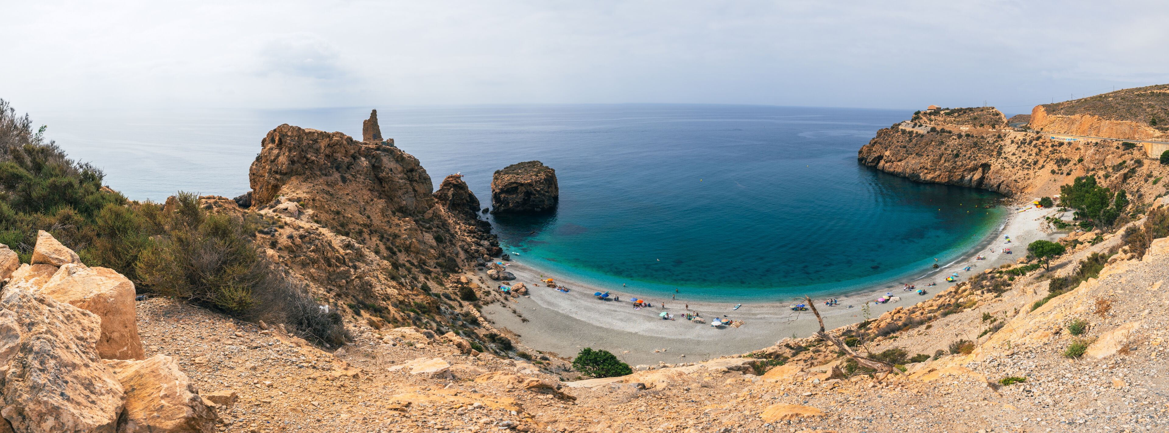 A coastal landscape with rocky cliffs, a sandy beach, and clear blue waters.