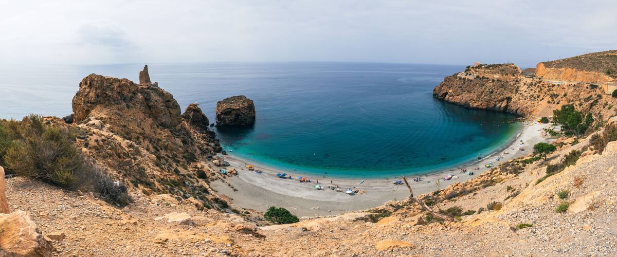 A coastal landscape with rocky cliffs, a sandy beach, and clear blue waters.
