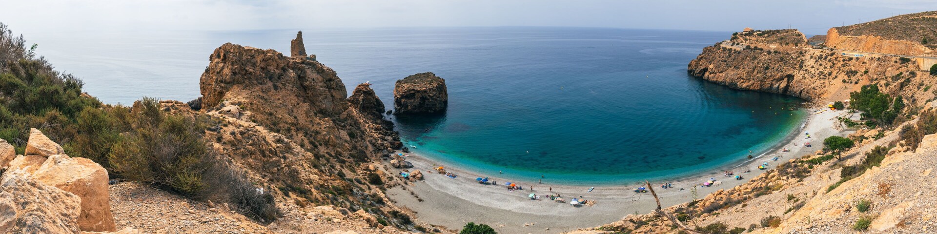 A coastal landscape with rocky cliffs, a sandy beach, and clear blue waters.