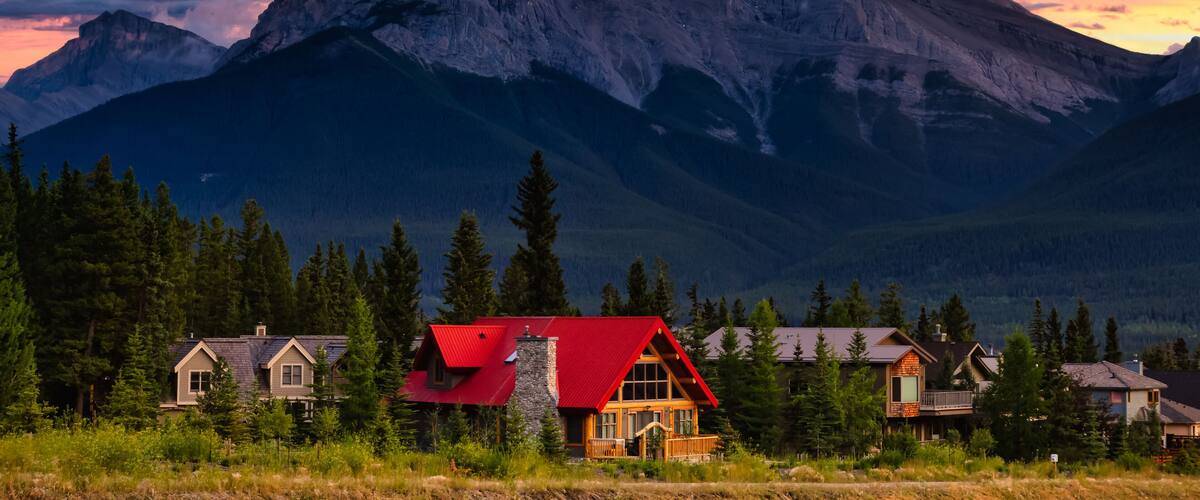 Une chaîne de montagnes avec un sommet imposant, un chalet au toit rouge et plusieurs autres maisons dans une vallée boisée.