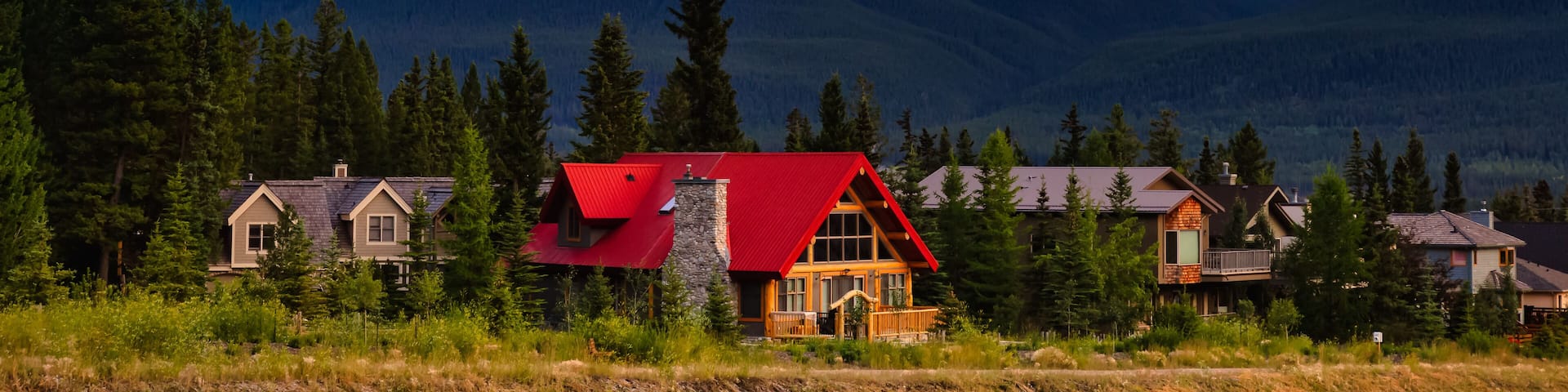 A mountain range with a prominent peak, a red-roofed cabin, and several other houses in a forested valley.