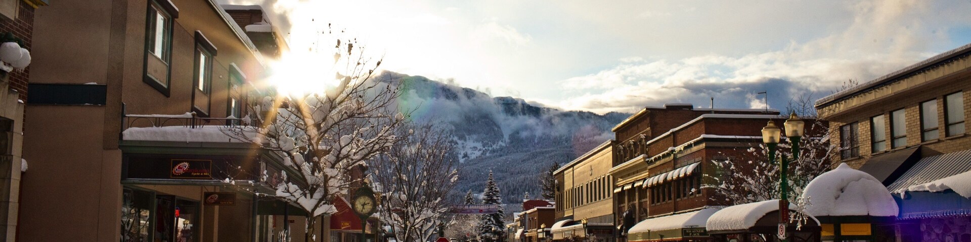 A snow-covered street with buildings, a stop sign, and a mountain in the background.