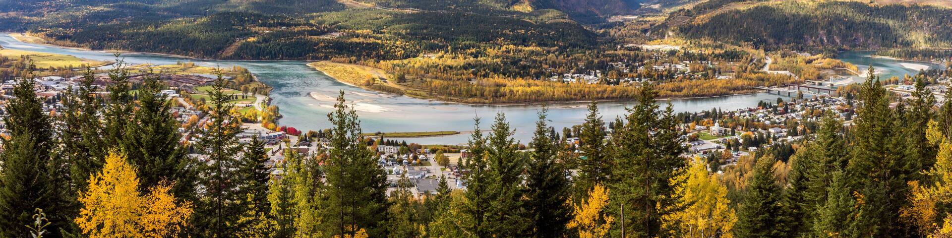 A mountainous landscape with a river, a town, and autumn foliage.