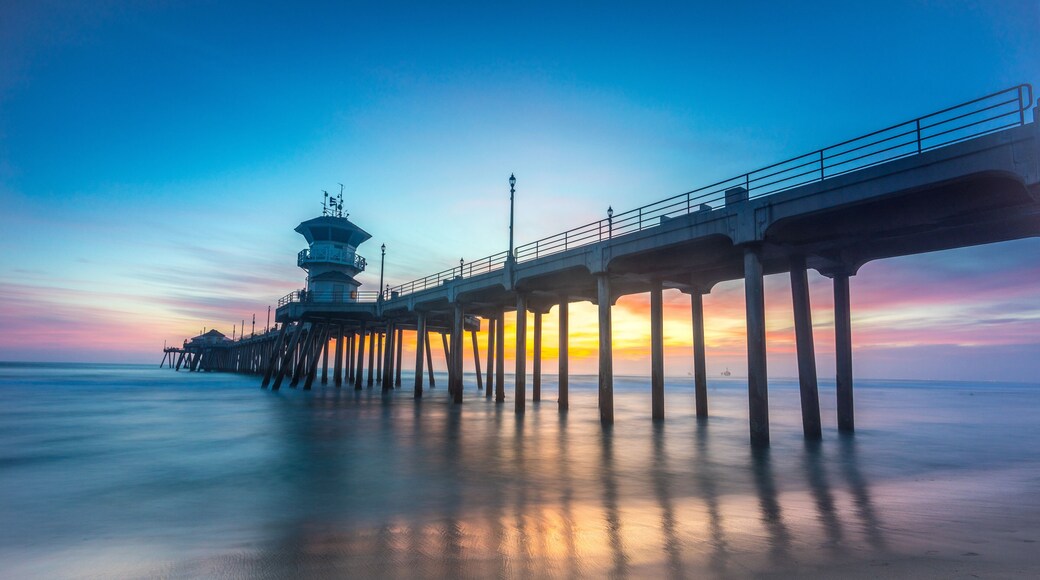 A pier extending into calm waters at sunset with a tower structure at the end.