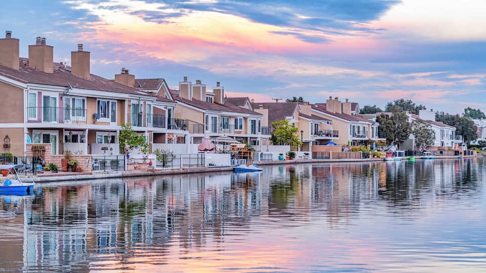 Homes in Huntington Beach with view of water reflecting cloudy sky at sunset