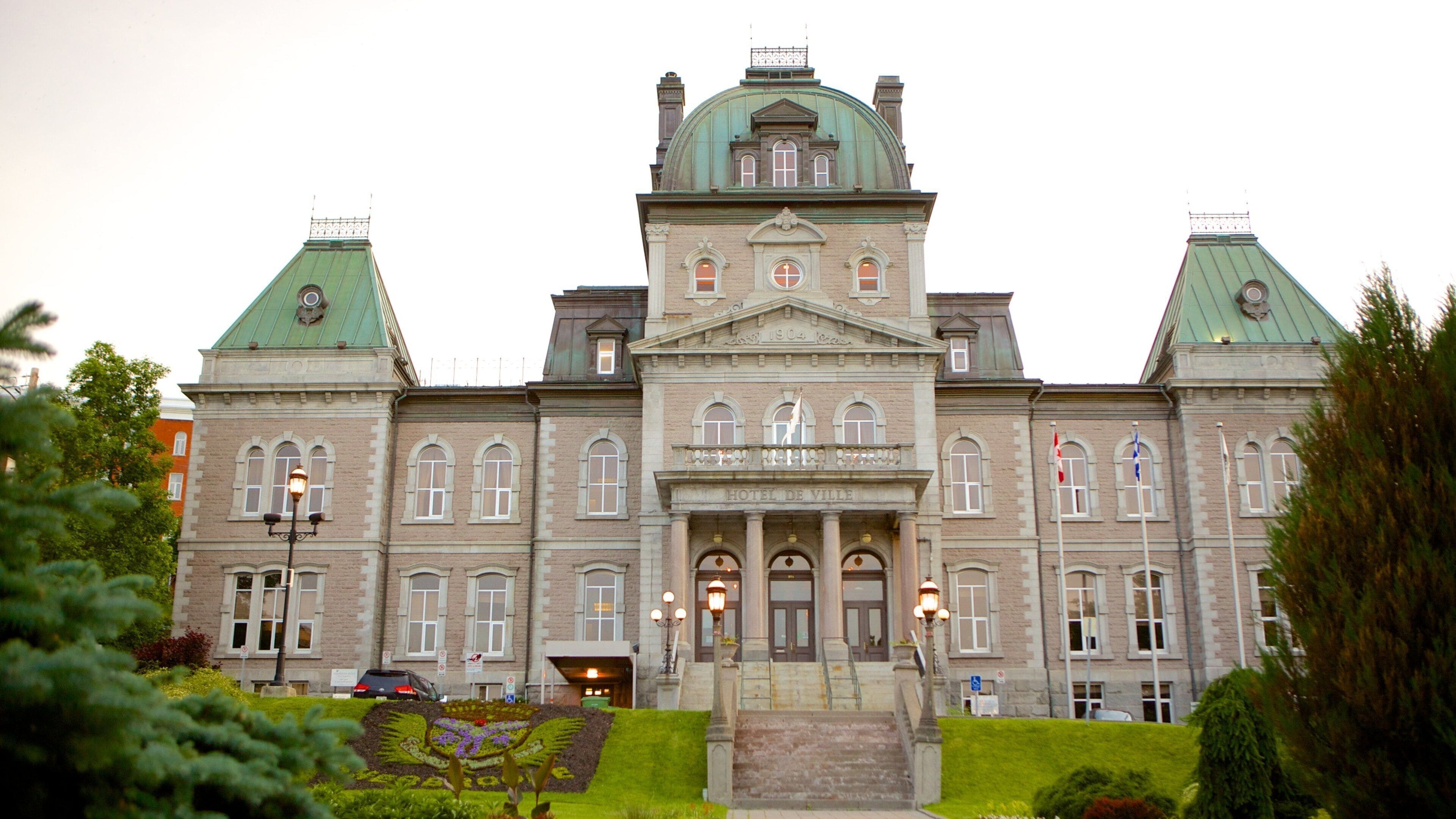 A large, historic building with a green dome and two smaller domes, surrounded by well-maintained gardens and trees.
