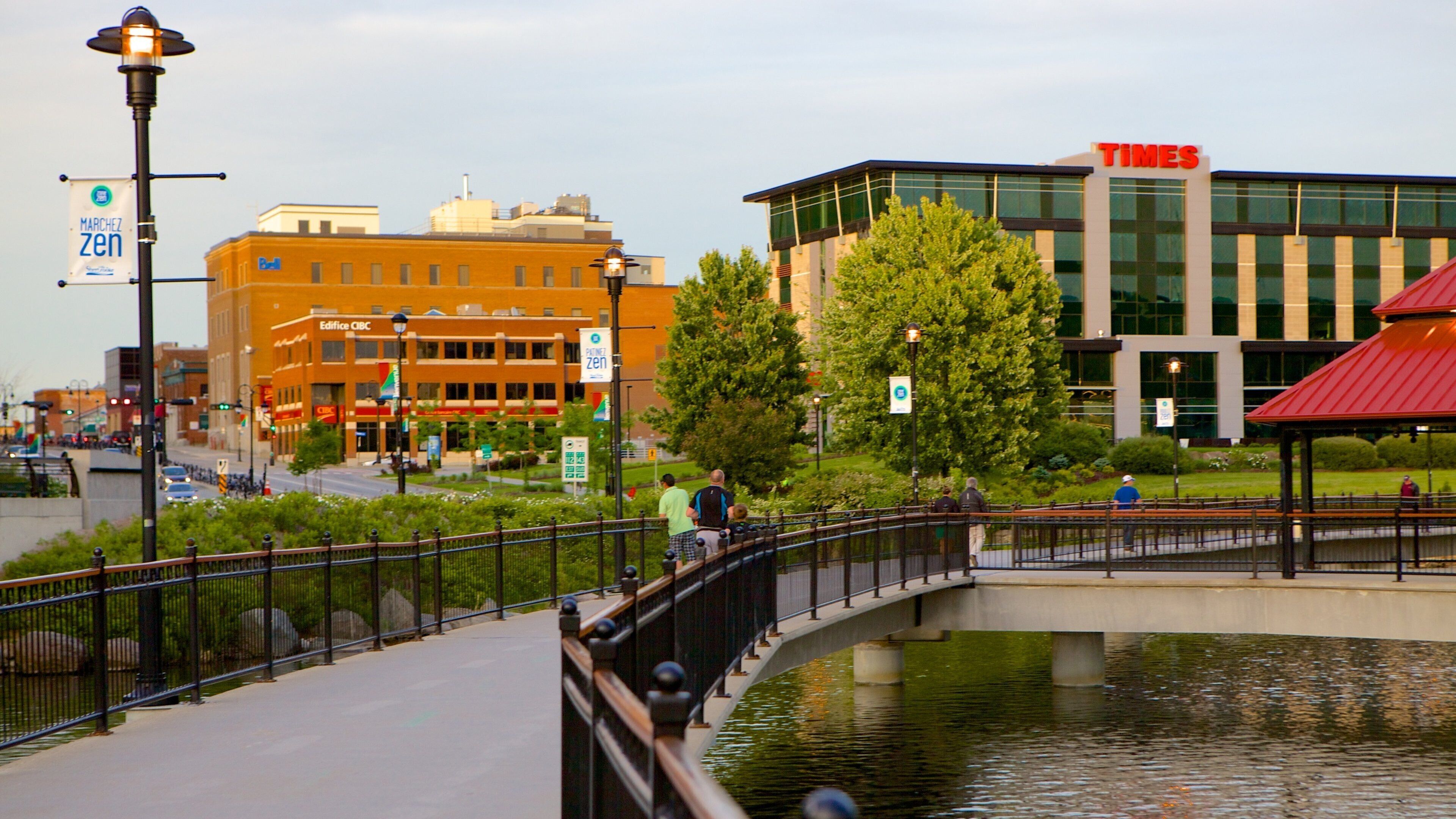 A pedestrian bridge over a canal with buildings, including a Times building, in the background.