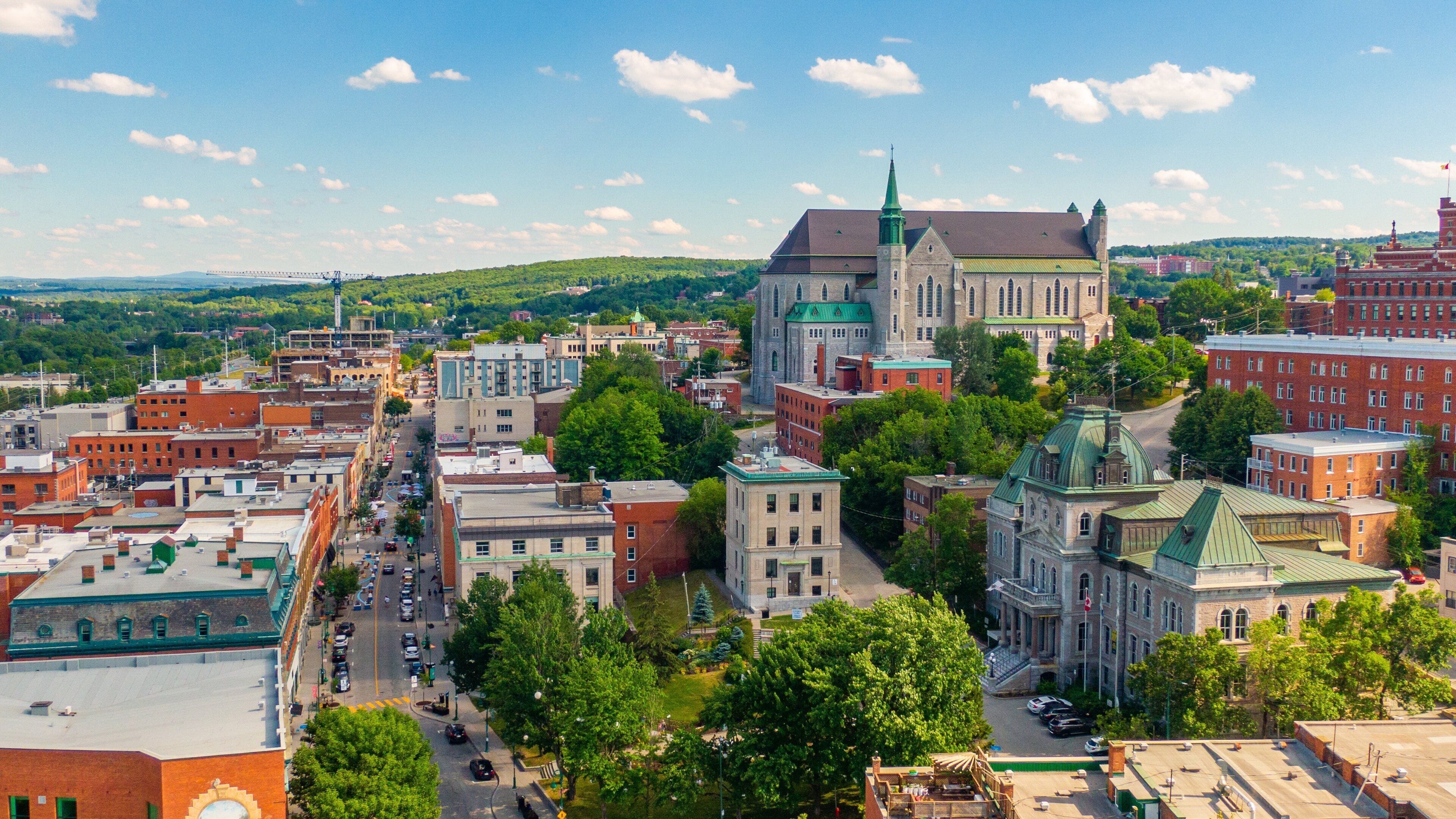 A cityscape with a prominent church with a green spire, surrounded by various buildings and a bridge in the distance.