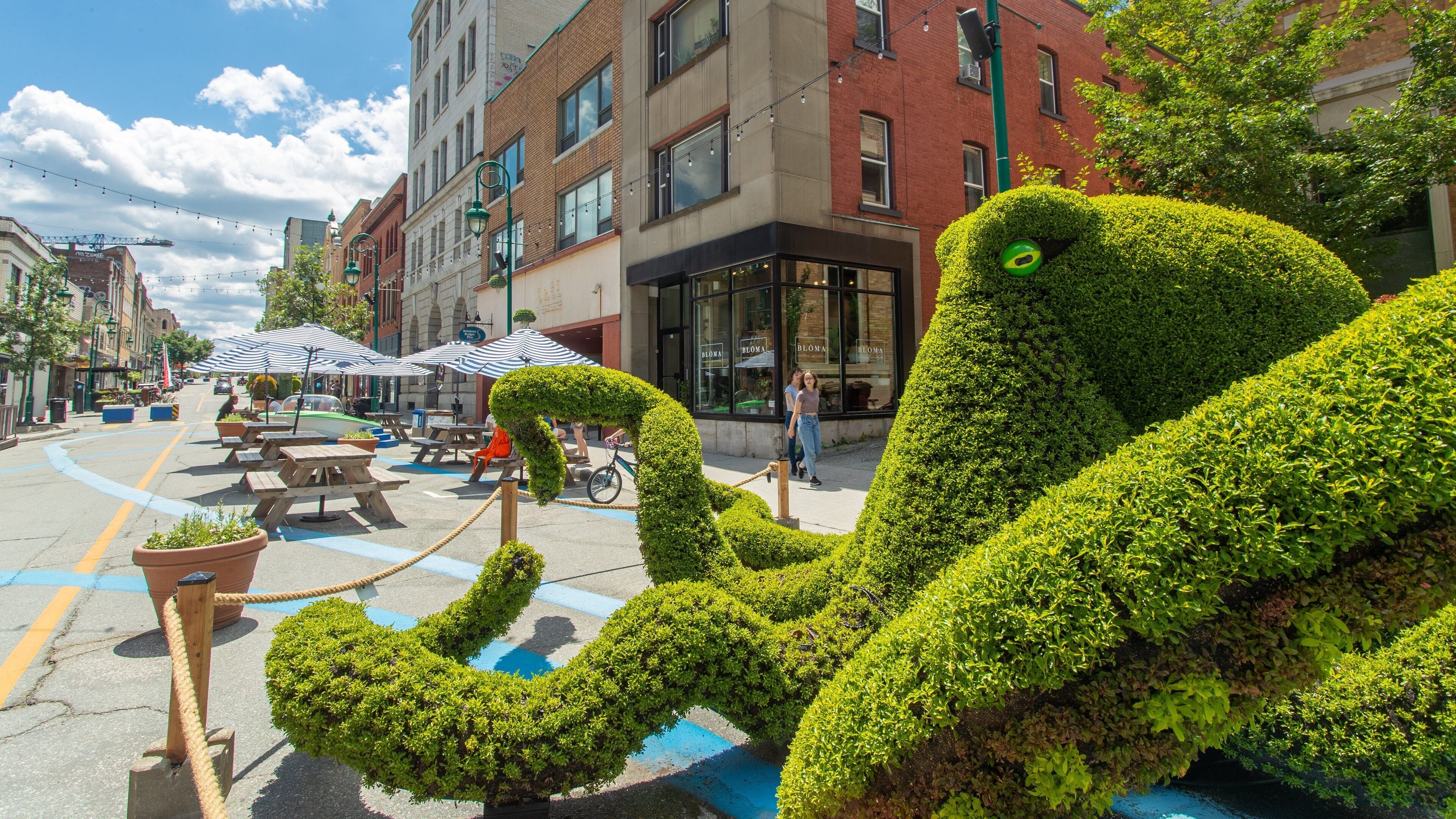 A street with a large octopus sculpture, outdoor seating, and buildings in the background.