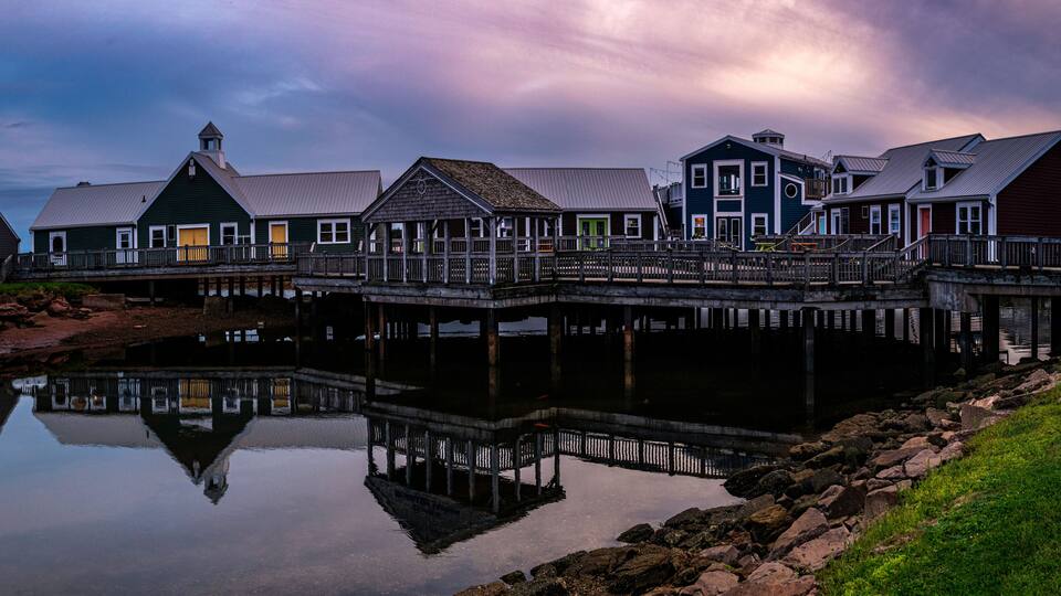 A waterfront with a row of multi-story buildings, a wooden pier, and a calm body of water reflecting the structures.