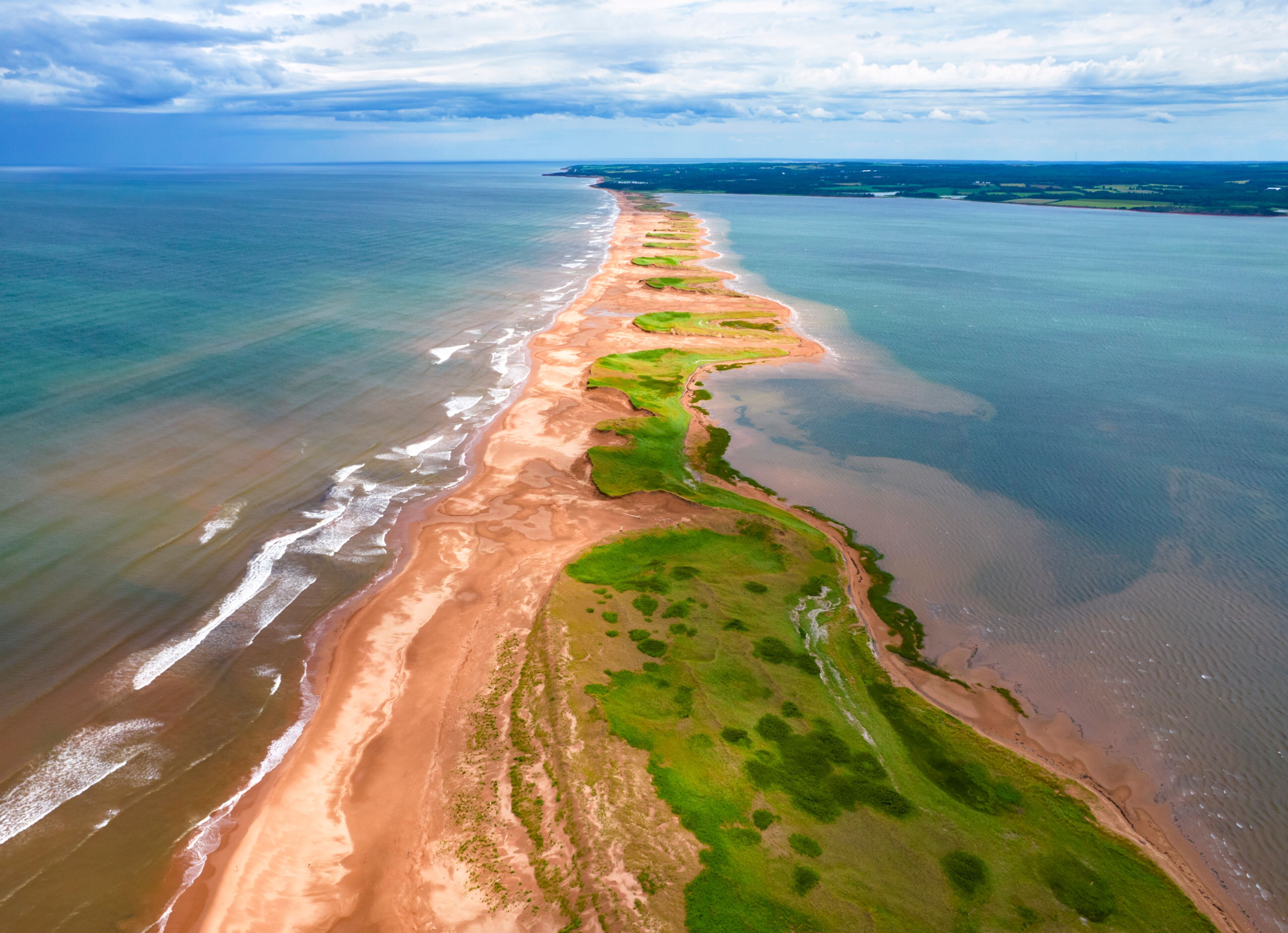 A coastal landscape with a sandy beach, green vegetation, and a clear view of the ocean.