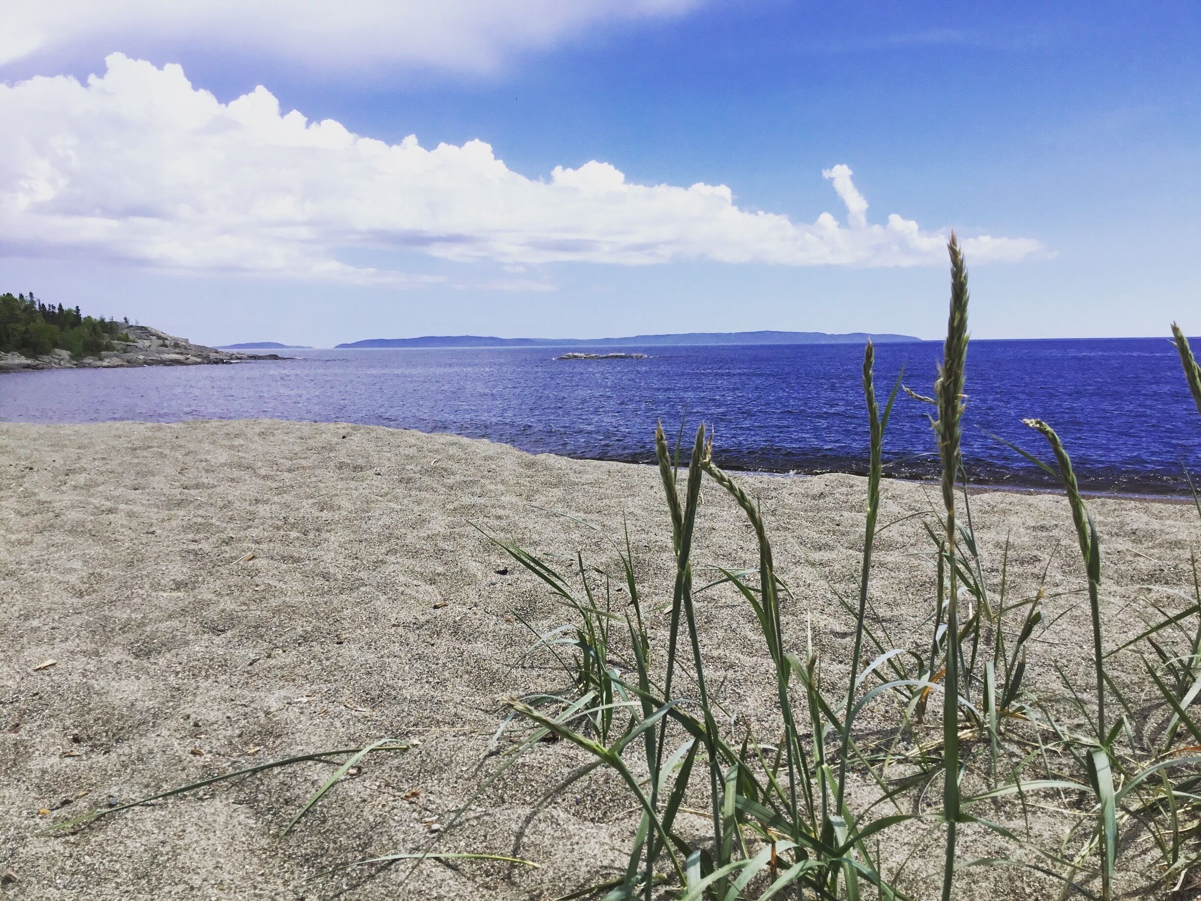 A beach with sand, grass, and a blue sea under a partly cloudy sky.