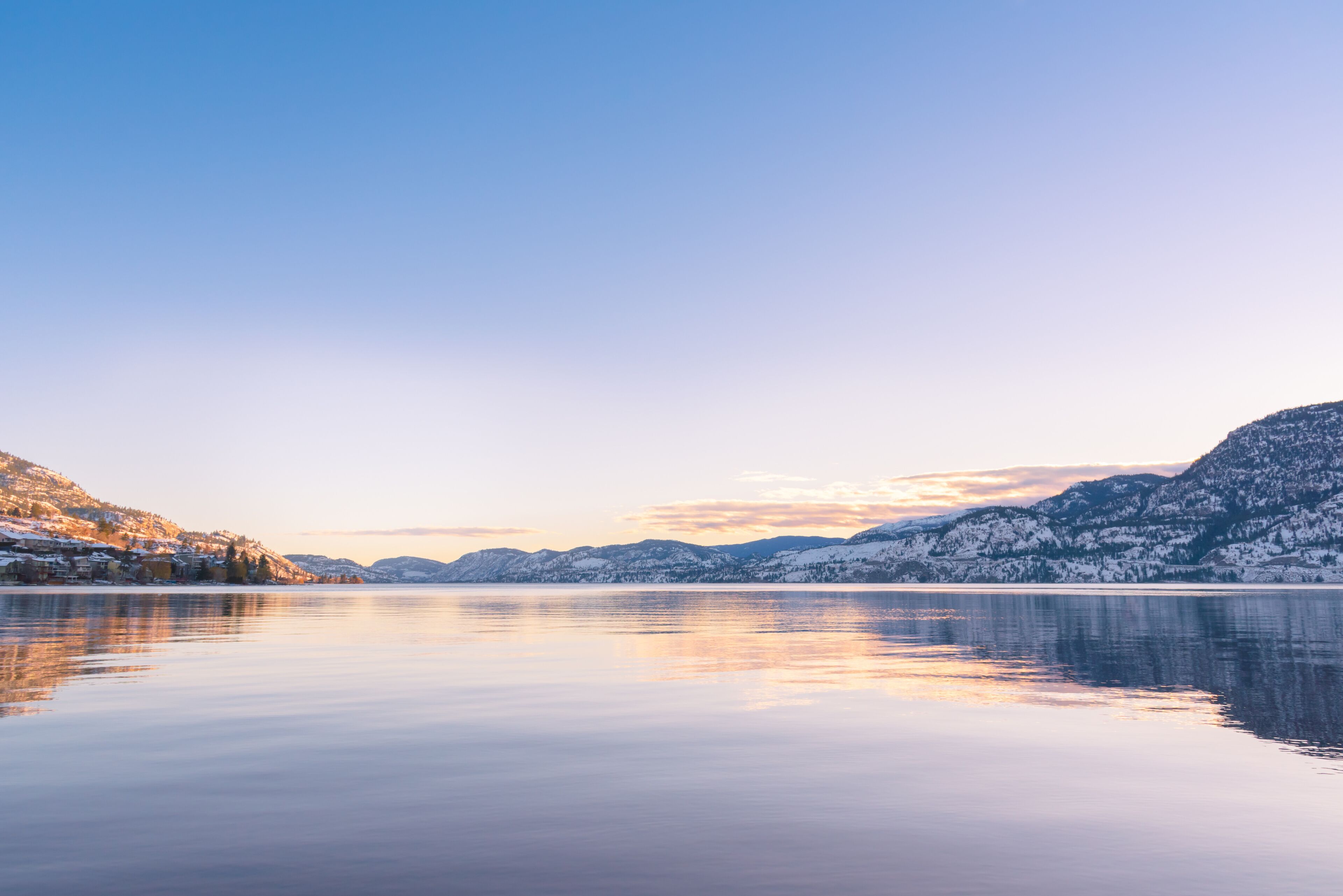 Um lago calmo refletindo montanhas cobertas de neve sob um céu claro.
