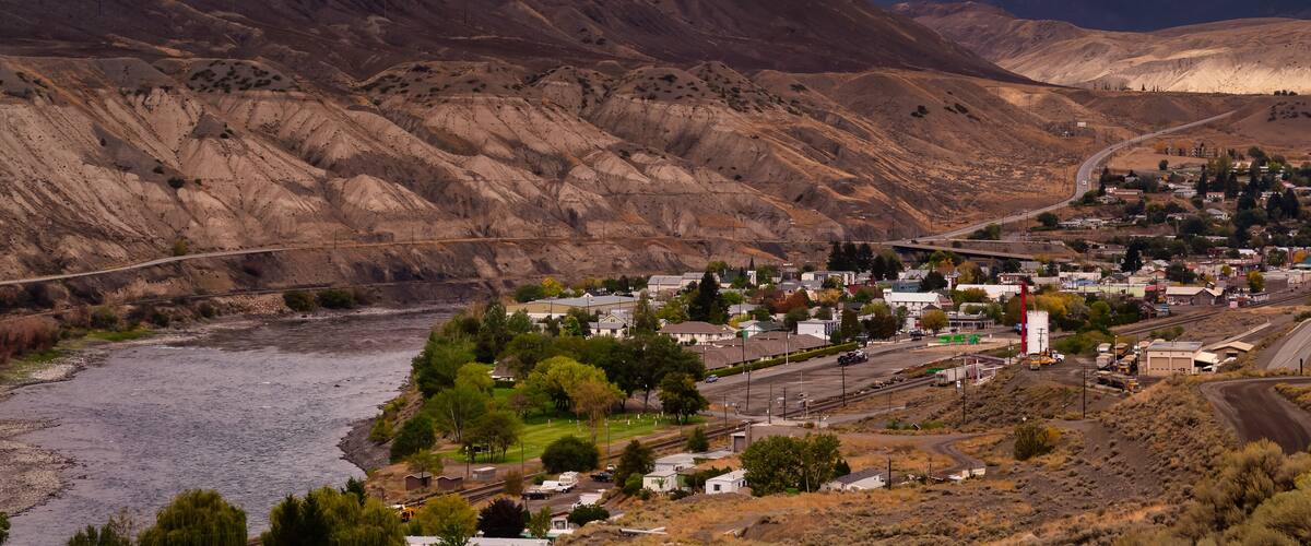 A town nestled in a valley with a river, surrounded by mountains and a bridge.