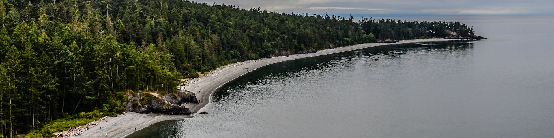 A curving shoreline with a forested island in the distance and calm waters.
