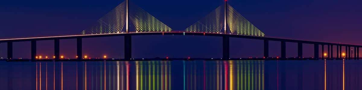 Un pont doté de deux tours et illuminé de lumières colorées qui se reflètent sur l’eau.