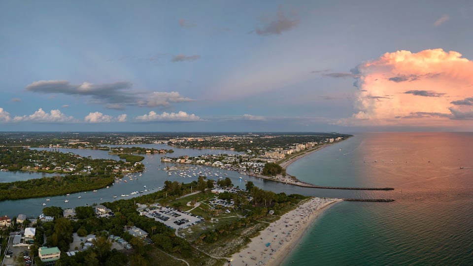 An aerial view of a coastal city with a marina, a beach, and a large cloud formation.