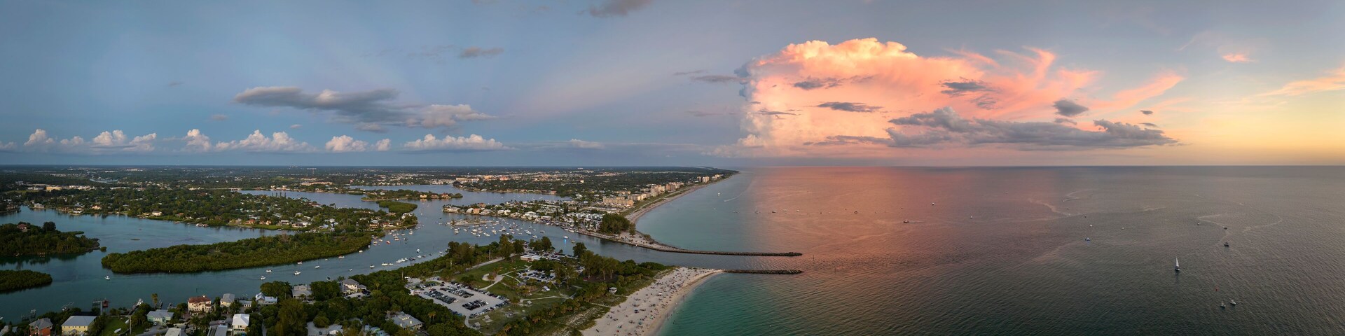 Vista aérea de una ciudad costera con un puerto deportivo, una playa y una gran formación de nubes.