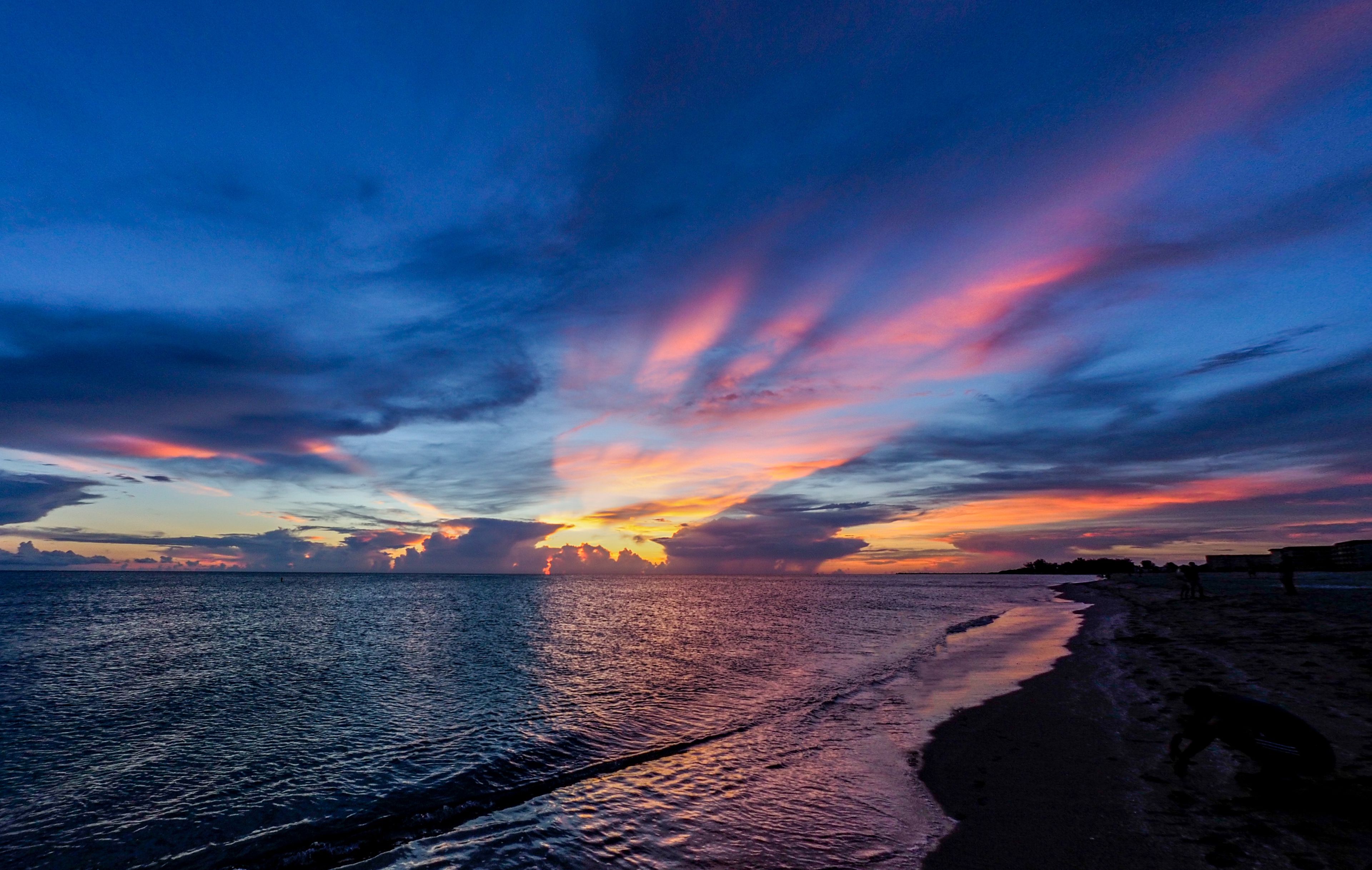A beach at sunset with a vibrant sky and calm sea.