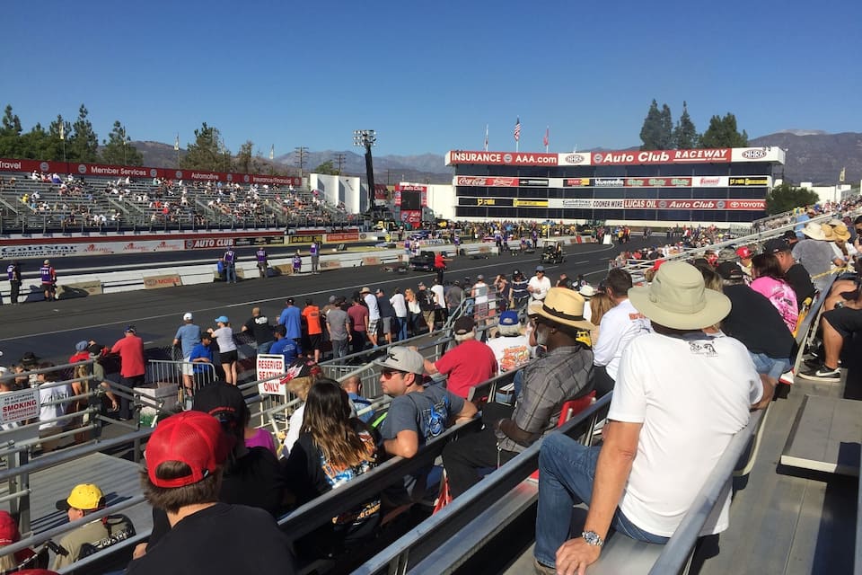 A crowded auto racing event with a track, spectators, and a large billboard advertising various sponsors.