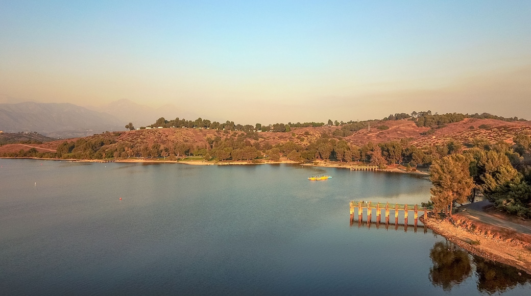 a stunning aerial shot of the still blue waters, the pier, the lush green trees and majestic mountain ranges at Puddingstone Lake in San Dimas California USA