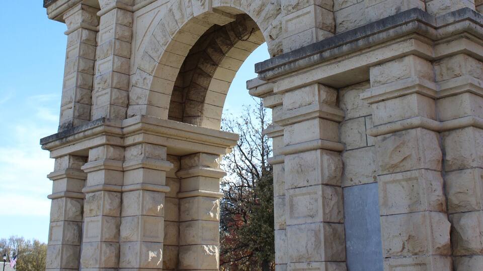 A large stone archway with intricate carvings and a statue on top.