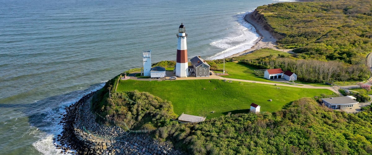 A lighthouse on a rocky outcrop with a grassy area and buildings nearby.