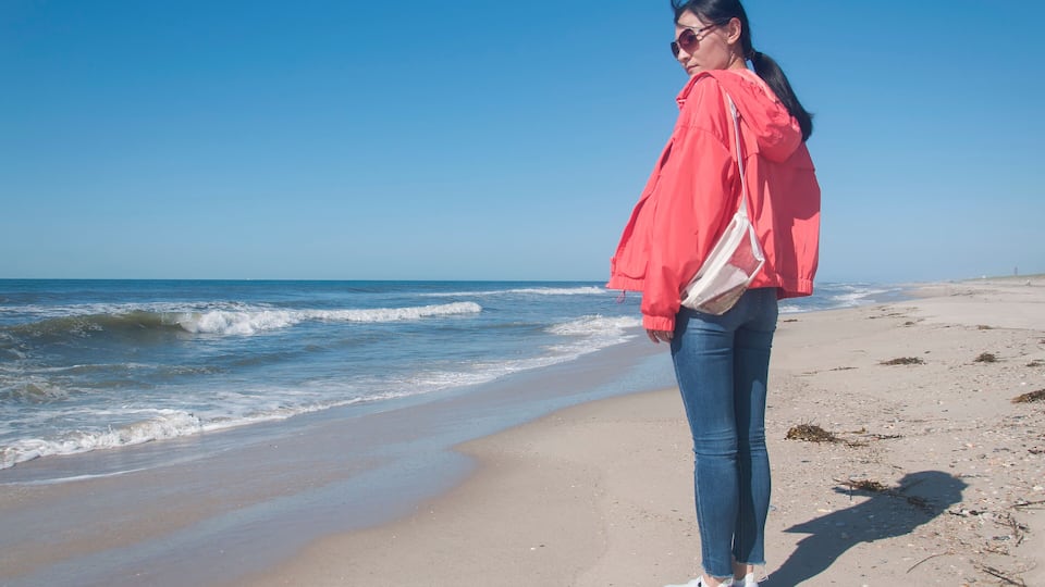 A beach with waves, a clear sky, and a person in a red jacket and jeans.