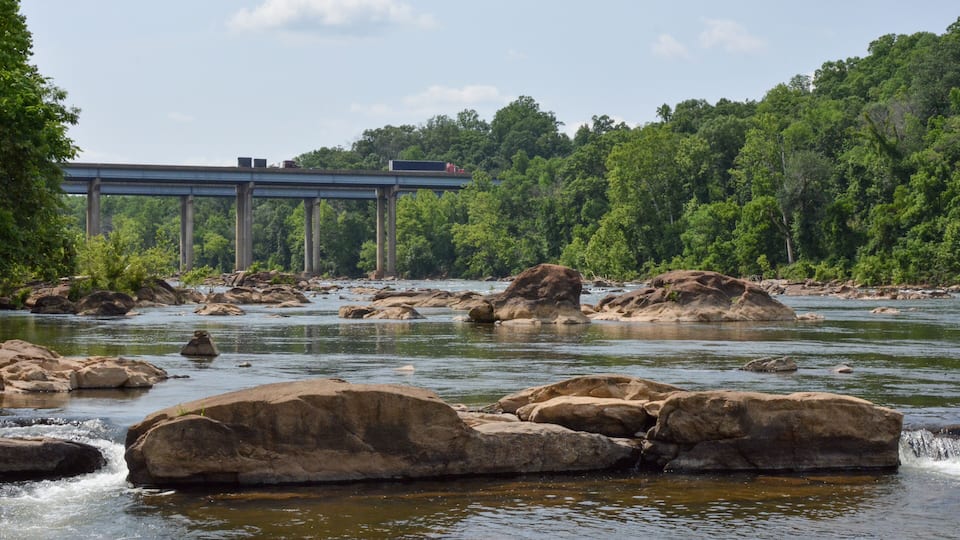 A river with large rocks, a bridge, and dense forest.