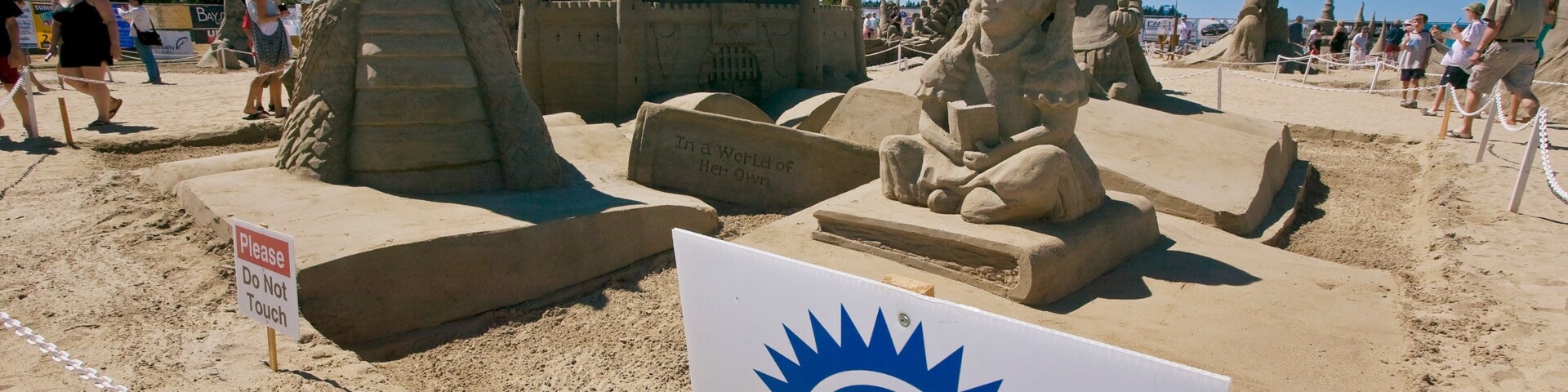 Competição de castelos de areia com uma placa indicando '1º Lugar'.