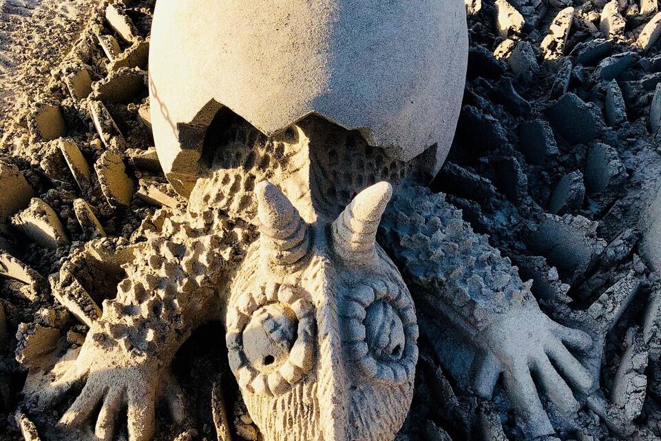 A sand sculpture of a creature with a large head and multiple arms.