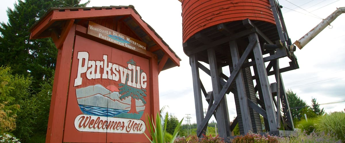 Un senyal de fusta vermell amb la paraula 'Parksville' i 'Benvinguts' escrites, al costat d'una torre d'aigua.