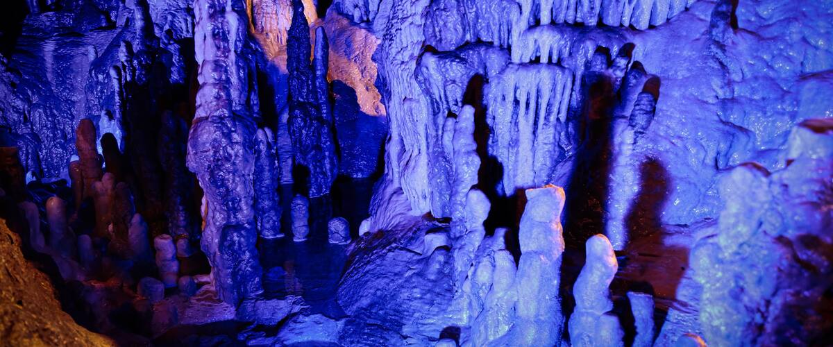 A cave with stalactites and stalagmites illuminated by blue lighting.