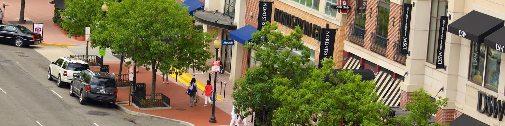 A street lined with various shops including a restaurant, a parking sign, and a building with a sign that reads "Marshalls".