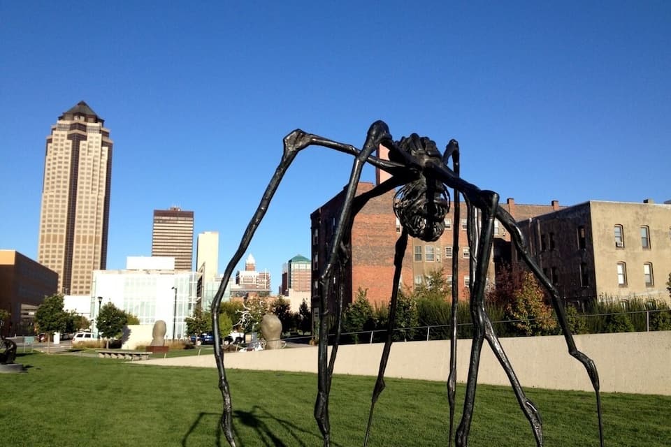 A sculpture of a large spider in a grassy park with a city skyline in the background.