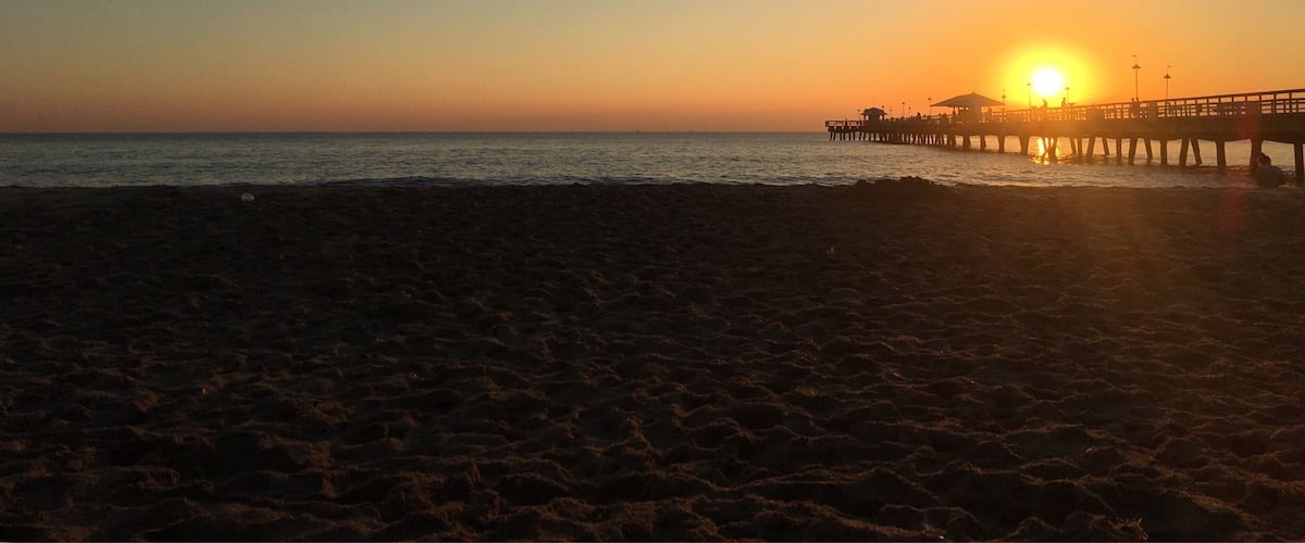 A beach at sunset with a pier extending into the water.