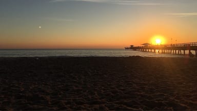 Uma praia ao pôr do sol, com um cais se estendendo na água.