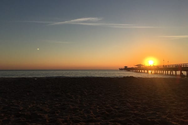 A beach at sunset with a pier extending into the water.