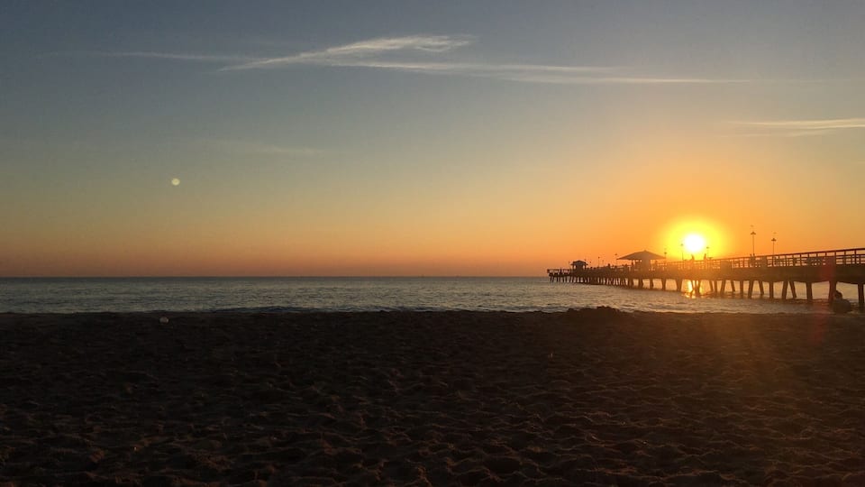 A beach at sunset with a pier extending into the water.