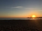 A beach at sunset with a pier extending into the water.
