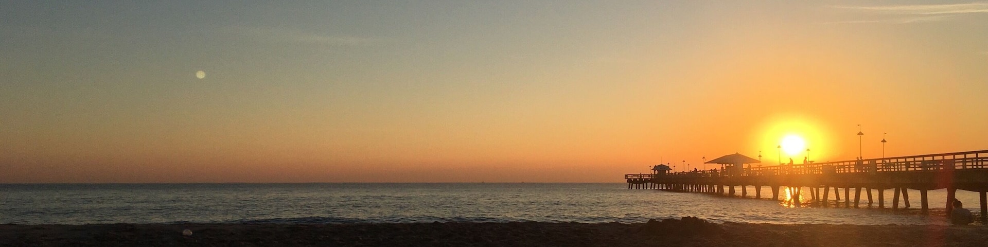 Una playa al atardecer con un muelle que se adentra en el agua.