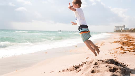 Side view of boy jumping at beach against cloudy sky