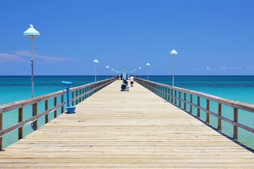 A wooden pier extending into turquoise waters, lined with evenly spaced street lamps.