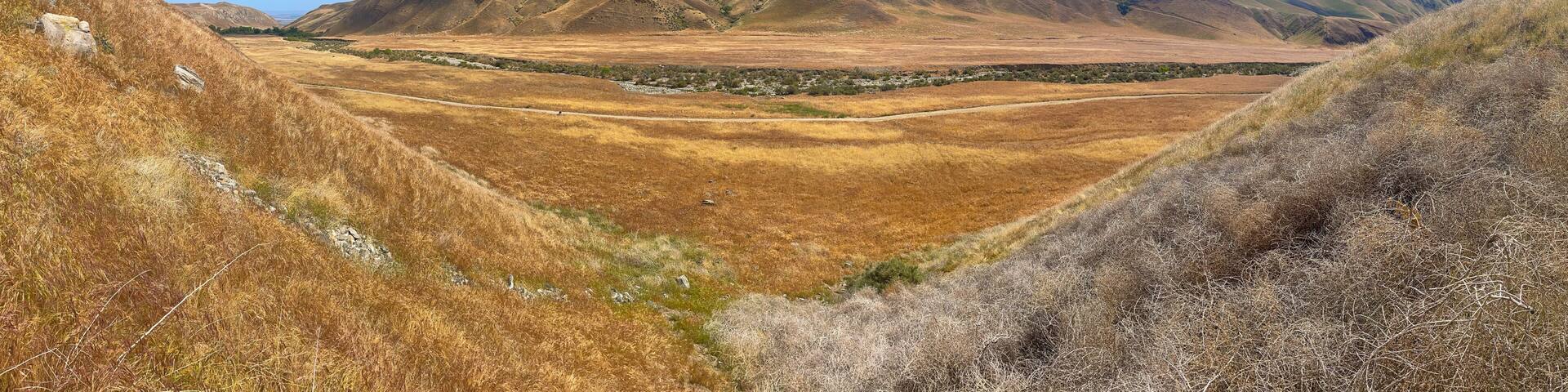 A dry valley with mountains in the background and a clear blue sky.