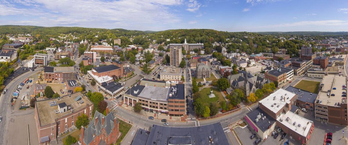 A town with a mix of historic and modern buildings, a prominent church, and surrounding green hills.