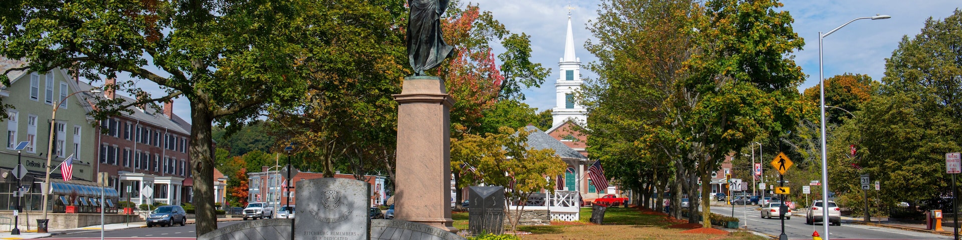 Una estatua conmemorativa en un parque con árboles e iglesia al fondo.