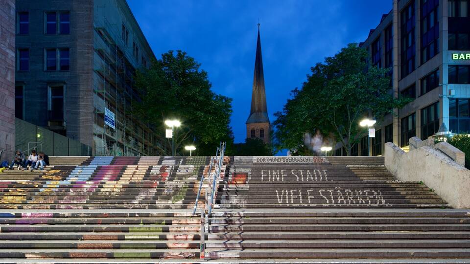 A cityscape with a church spire, steps with graffiti, and modern buildings.