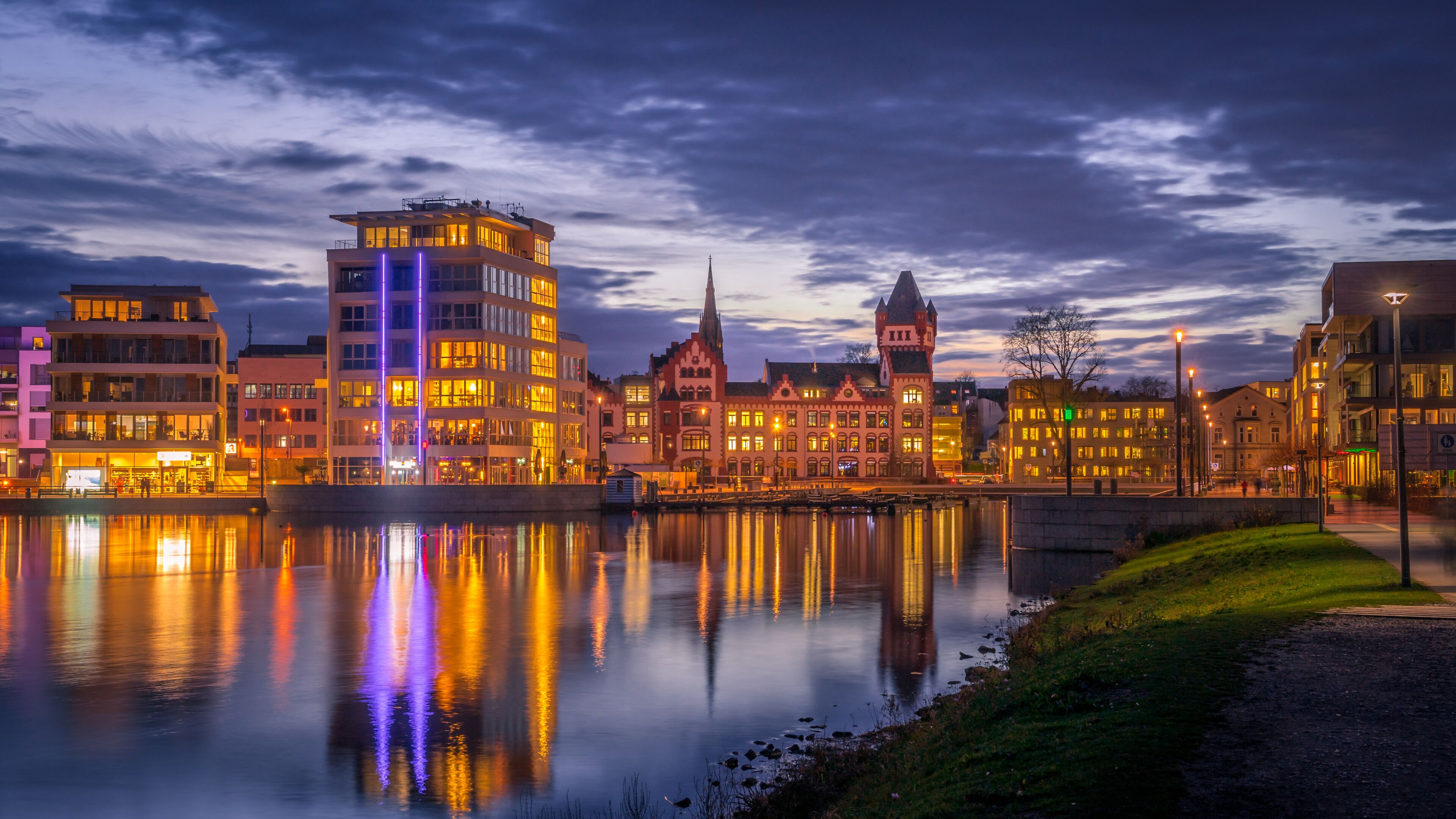 A cityscape with a river reflecting buildings, including a tower and a church with a spire.