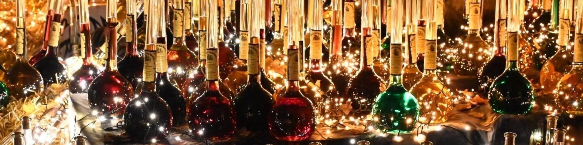 A collection of wine bottles and glassware, illuminated by string lights.